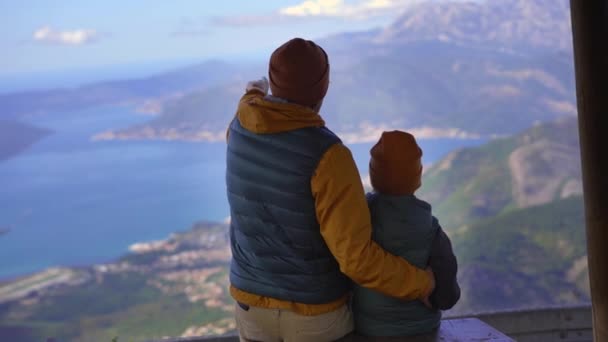 Un padre y un hijo viajan a Montenegro en otoño. Miran la bahía de Boka Kotorska desde un punto de vista en una montaña — Vídeos de Stock