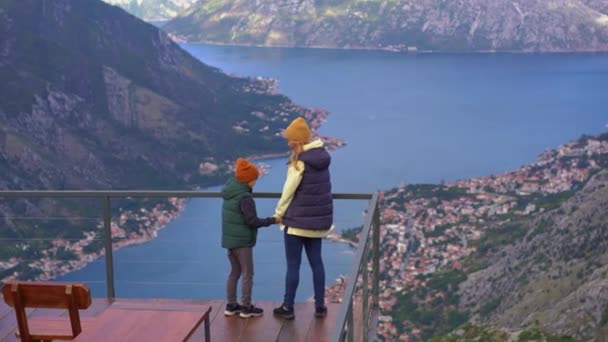 Een moeder en zoon reizen in het najaar in Montenegro. Ze kijken naar de Boka Kotorska baai vanaf een uitkijkpunt op een berg — Stockvideo