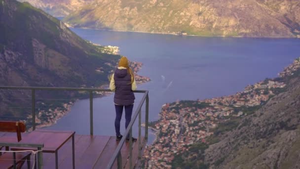 Una mujer viaja a Montenegro en otoño. Ella mira la bahía de Boka Kotorska desde un punto de vista en una montaña — Vídeo de stock