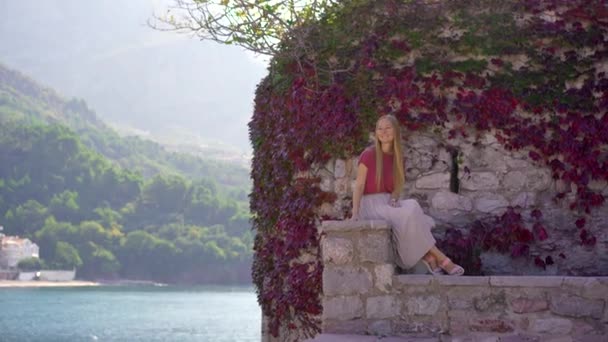 Handheld shot. A woman traveler visits the Sveti Stefan island. Famous tourist location near the city of Budva. Travel to Montenegro concept — Vídeo de Stock