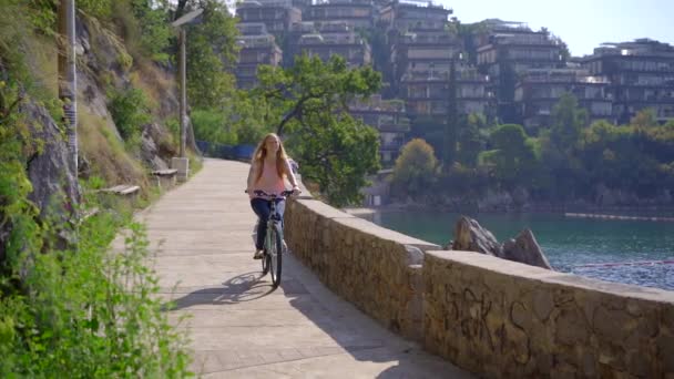 Fotografía en cámara lenta de una joven que monta en bicicleta en la ciudad de Budva, un famoso lugar turístico en Montenegro. Viajes a Montenegro concepto — Vídeos de Stock