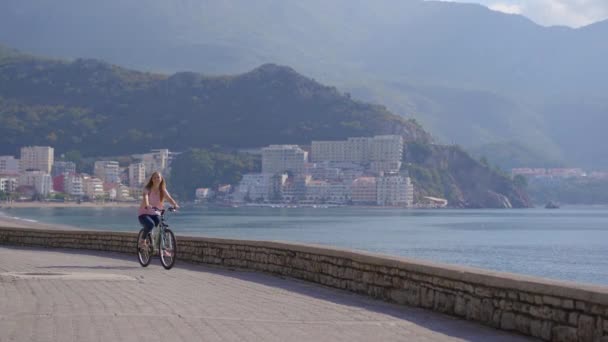 Een jonge vrouw fietst in de stad Budva, een beroemde toeristische plaats in Montenegro. Reizen naar Montenegro — Stockvideo