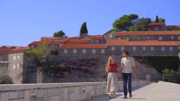Um homem e uma mulher viajantes visitam a ilha Sveti Stefan. Famosa localização turística perto da cidade de Budva. Viajar para Montenegro conceito. — Vídeo de Stock