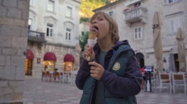 Küçük çocuk Karadağ 'ın eski Kotor kasabasında bir meydanda dikilmiş çikolatalı dondurma yiyor. Karadağ 'a seyahat. Bir dünya mirası alanı. El kamerasıyla.