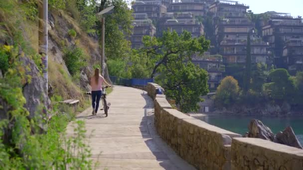 Una joven monta en bicicleta en la ciudad de Budva, un famoso lugar turístico en Montenegro. Viajes a Montenegro concepto — Vídeos de Stock