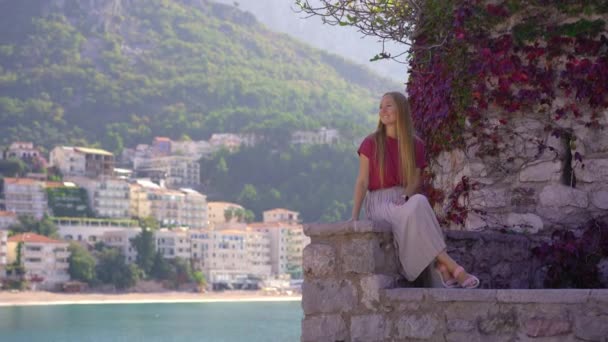 Um tiro à mão. Uma mulher viajante visita a ilha Sveti Stefan. Famosa localização turística perto da cidade de Budva. Viajar para Montenegro conceito — Vídeo de Stock