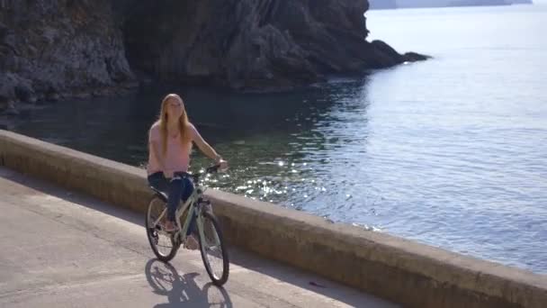 Una joven monta en bicicleta en la ciudad de Budva, un famoso lugar turístico en Montenegro. Viajes a Montenegro concepto — Vídeos de Stock