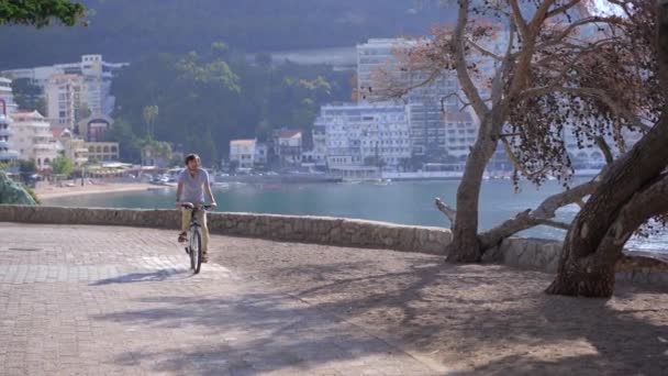 Un joven monta en bicicleta en la ciudad de Budva, un famoso lugar turístico en Montenegro. Viajes a Montenegro concepto — Vídeos de Stock