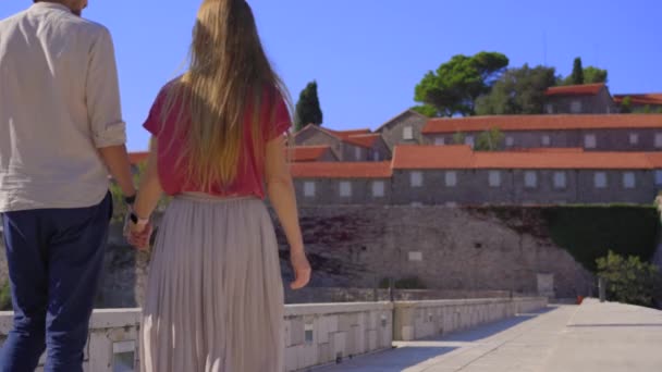 A man and a woman travelers visit the Sveti Stefan island. Famous tourist location near the city of Budva. Travel to Montenegro concept. — Stock video