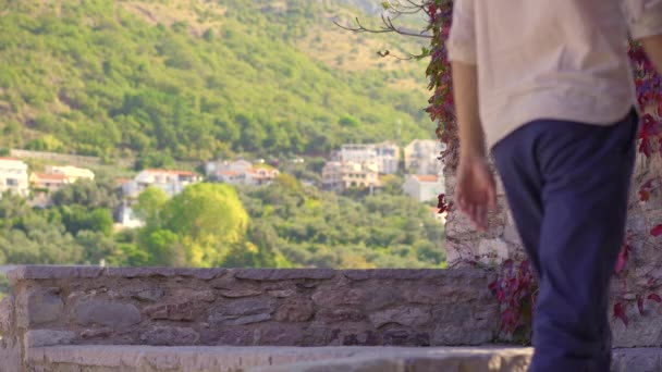 Ένας άνδρας και μια γυναίκα ταξιδιώτες επισκέπτονται το νησί Σβέτι Στεφάν. Διάσημη τουριστική τοποθεσία κοντά στην πόλη Μπούντβα. Ταξίδι στο Μαυροβούνιο. — Αρχείο Βίντεο