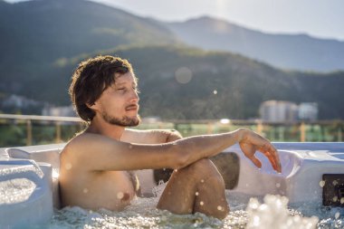 Genç, tasasız, mutlu, gülümseyen bir adamın portresi. Jakuzinin keyfini çıkarırken yeşil büyük dağların arka planında seyahat eden mutlu bir tatil hayatı.
