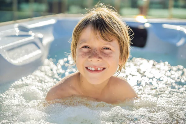Retrato de un joven niño feliz y despreocupado que se relaja en la bañera de hidromasaje mientras disfruta de unas felices vacaciones en un momento de viaje. La vida en el fondo de grandes montañas verdes —  Fotos de Stock
