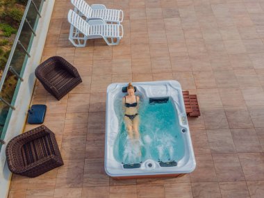 İHA görüntüsü. Genç kaygısız mutlu kadının portresi jakuzide rahatlayarak yeşil büyük dağların arka planında mutlu bir tatil hayatı yaşıyor.