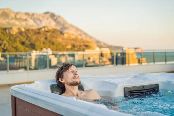 Portrait of young carefree happy smiling man relaxing at hot tub during enjoying happy traveling moment vacation life against the background of green big mountains — Zdjęcie stockowe