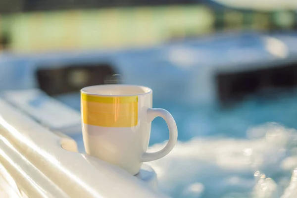 Mug with morning drink on the side of Hot tub hydromassage pool. Illuminated pool. Rest outside the city. Cottage with hydromassage pool — Stock fotografie