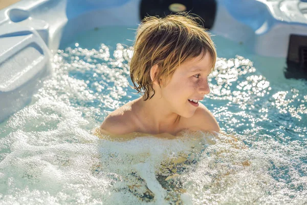 Retrato de un joven niño feliz y despreocupado que se relaja en la bañera de hidromasaje mientras disfruta de unas felices vacaciones en un momento de viaje. La vida en el fondo de grandes montañas verdes —  Fotos de Stock