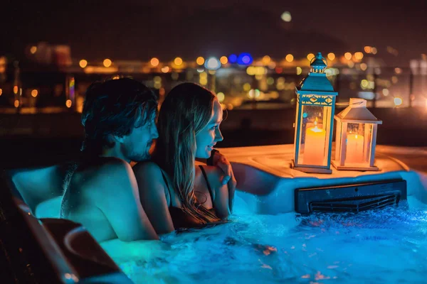 Portrait of young carefree happy smiling couple relaxing at hot tub during enjoying happy traveling moment vacation life against the background of green big mountains at night — Stockfoto
