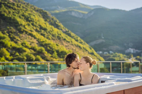 Retrato de joven despreocupada feliz pareja sonriente relajarse en la bañera de hidromasaje durante el disfrute de la vida feliz viaje momento de vacaciones en el fondo de grandes montañas verdes —  Fotos de Stock