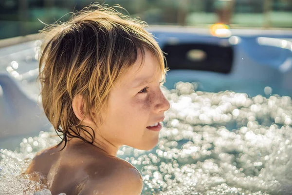 Retrato de un joven niño feliz y despreocupado que se relaja en la bañera de hidromasaje mientras disfruta de unas felices vacaciones en un momento de viaje. La vida en el fondo de grandes montañas verdes — Foto de Stock