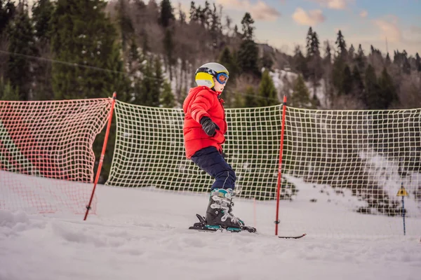 Criança a esquiar nas montanhas. Criança ativa com capacete de segurança, óculos e postes. Corrida de esqui para crianças pequenas. Desporto de inverno para a família. Aula de esqui para crianças na escola alpina. Pequena corrida de esqui na neve — Fotografia de Stock