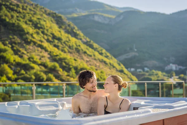 Retrato de joven despreocupada feliz pareja sonriente relajarse en la bañera de hidromasaje durante el disfrute de la vida feliz viaje momento de vacaciones en el fondo de grandes montañas verdes — Foto de Stock