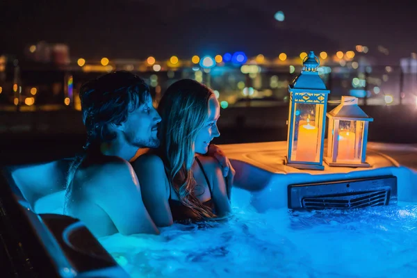 Retrato de joven despreocupada feliz pareja sonriente relajarse en la bañera de hidromasaje durante el disfrute de la vida feliz viaje momento de vacaciones en el fondo de grandes montañas verdes por la noche — Foto de Stock