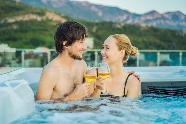 Retrato de jovem casal sorridente feliz despreocupado relaxando na banheira de hidromassagem durante a desfrutar de vida de férias momento de viagem feliz contra o fundo de verdes grandes montanhas — Fotografia de Stock