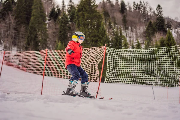 Criança a esquiar nas montanhas. Criança ativa com capacete de segurança, óculos e postes. Corrida de esqui para crianças pequenas. Desporto de inverno para a família. Aula de esqui para crianças na escola alpina. Pequena corrida de esqui na neve — Fotografia de Stock