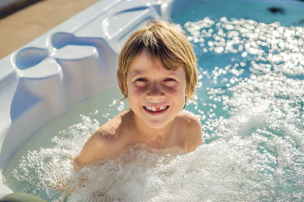 Retrato de un joven niño feliz y despreocupado que se relaja en la bañera de hidromasaje mientras disfruta de unas felices vacaciones en un momento de viaje. La vida en el fondo de grandes montañas verdes — Foto de Stock