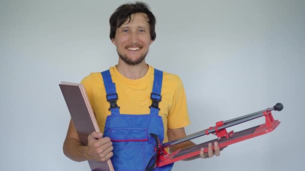 Een professionele tegelinstallateur houdt tegels en een tegelsnijmachine in zijn handen. Hij kijkt glimlachend naar de camera. — Stockvideo