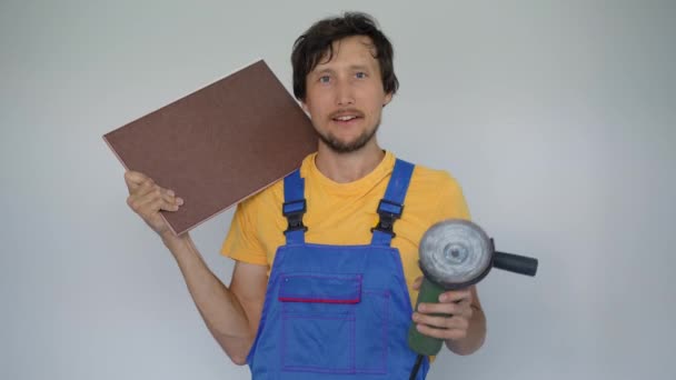 Een man professionele tegel installateur houdt een tegel en een hoek slijper zijn armen. Hij kijkt glimlachend naar de camera. — Stockvideo