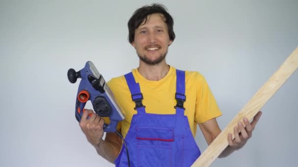 A man professional tile installer a wooden plank and an electric planer in his hands. He looks at the camera smiling — Stock Video