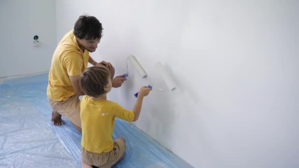 Отец и сын в жёлтой футболке красят стену роллером. Они ремонтируют свою квартиру. DIY концепция ремонта дома. Семейное время — стоковое видео