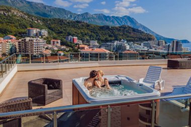 İHA görüntüsü. Genç kaygısız mutlu çiftin portresi jakuzide dinlenirken yeşil büyük dağların arka planında mutlu bir tatil hayatı yaşıyor.