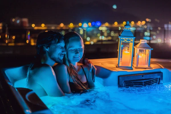 Retrato de joven despreocupada feliz pareja sonriente relajarse en la bañera de hidromasaje durante el disfrute de la vida feliz viaje momento de vacaciones en el fondo de grandes montañas verdes por la noche — Foto de Stock
