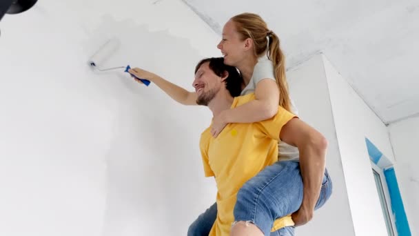 Un hombre y una mujer felices pintan la pared usando un pintor de rodillos. Están renovando su apartamento. Concepto de renovación del hogar DIY. Tiempo en familia. Disparo en cámara lenta — Vídeo de stock