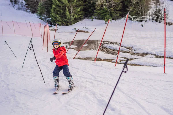 Ski d'enfant en montagne. Enfant tout-petit actif avec casque de sécurité, lunettes et bâtons. Course de ski pour jeunes enfants. Sport d'hiver pour la famille. Cours de ski pour enfants à l'école de ski alpin. Petit skieur de course dans la neige — Photo