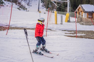 Çocuk dağlarda kayak yapıyor. Güvenlik kaskı, gözlüğü ve direkleri olan aktif bir çocuk. Küçük çocuklar için kayak yarışı. Aile için kış sporu. Alp okulunda çocuklar kayak dersi alıyor. Küçük kayakçı karda yarışıyor