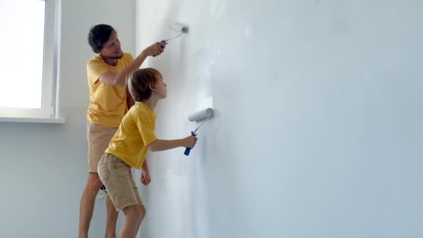 Ein Vater und sein Sohn tragen beide ein gelbes T-Shirt und bemalen die Wand mit einem Rollenmaler. Sie renovieren gerade ihre Wohnung. Heimwerker-Konzept. Familienzeit. Zeitlupenschuss — Stockvideo