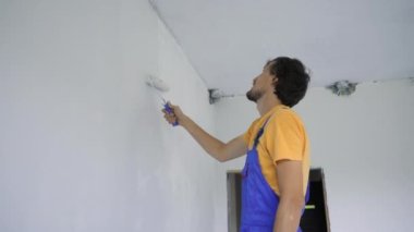 Profesyonel bir inşaat işçisi paten boyacısı kullanarak duvarı boyuyor.