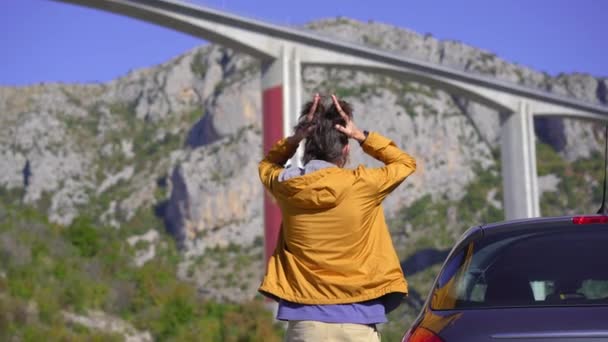 Ein Mann, der neben seinem Auto steht, blickt auf die Moracica-Brücke in Montenegro. Er ist schockiert von der Nachricht, wie teuer diese Brücke ist und wie viel Geld Montenegro China schuldet — Stockvideo