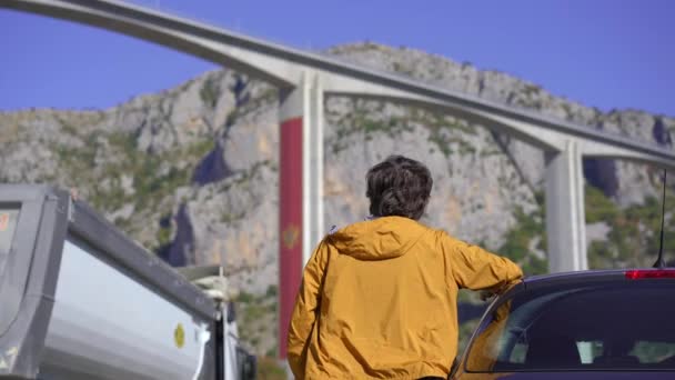 彼の車のそばに立っている男はモンテネグロのモラシカ橋を見ている。モンテネグロを車で旅行中だ — ストック動画