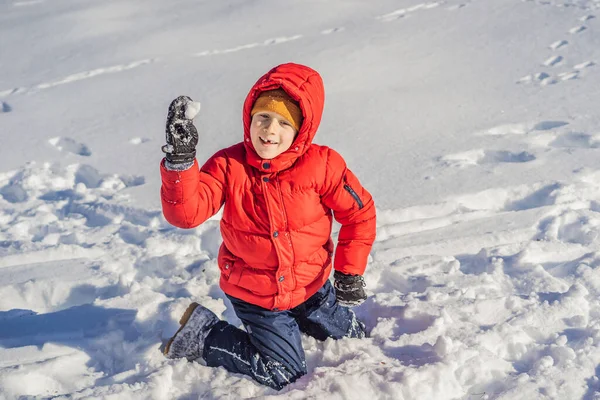 青い冬の服を着た面白い男の子が雪の中を歩く。子供のための屋外冬の活動。かわいい子供を身に着けている暖かい帽子低い彼の目の上に雪の結晶をキャッチ彼の舌 — ストック写真