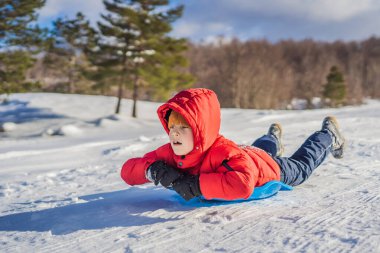 Mutlu ve pozitif küçük çocuk kızakla kaymayı ve soğuk havayı seviyor. Kış eğlencesi konsepti.