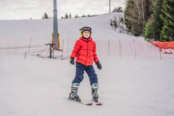 Criança a esquiar nas montanhas. Criança ativa com capacete de segurança, óculos e postes. Corrida de esqui para crianças pequenas. Desporto de inverno para a família. Aula de esqui para crianças na escola alpina. Pequena corrida de esqui na neve — Fotografia de Stock