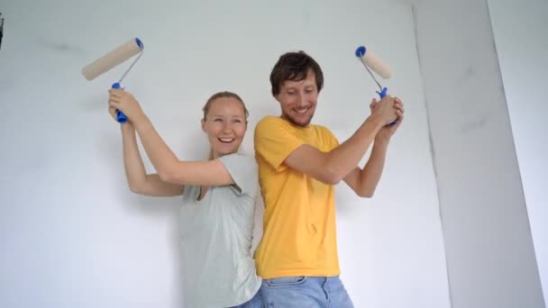 一个快乐的男人和女人用滚筒油漆刷墙壁.他们正在整修他们的公寓。DIY家庭翻新概念。家庭时间。慢动作射击 — 图库视频影像