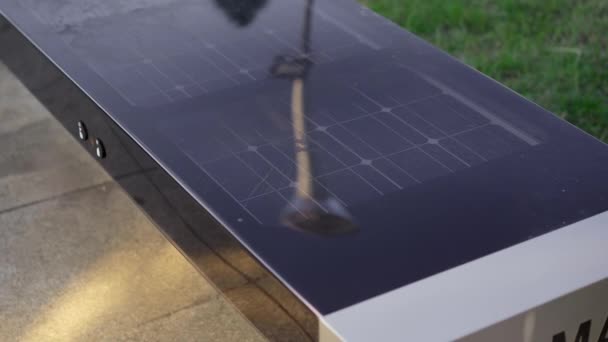 En smart benk med smarttelefon på. En smartbenk har solcellepaneler på toppen og kan lade USB-enheter gratis – stockvideo