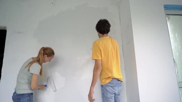 Un hombre y una mujer felices pintan la pared usando un pintor de rodillos. Están renovando su apartamento. Concepto de renovación del hogar DIY. Tiempo en familia. Disparo en cámara lenta — Vídeos de Stock