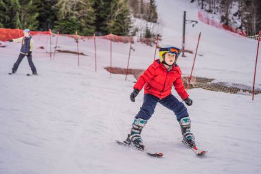 Çocuk dağlarda kayak yapıyor. Güvenlik kaskı, gözlüğü ve direkleri olan aktif bir çocuk. Küçük çocuklar için kayak yarışı. Aile için kış sporu. Alp okulunda çocuklar kayak dersi alıyor. Küçük kayakçı karda yarışıyor