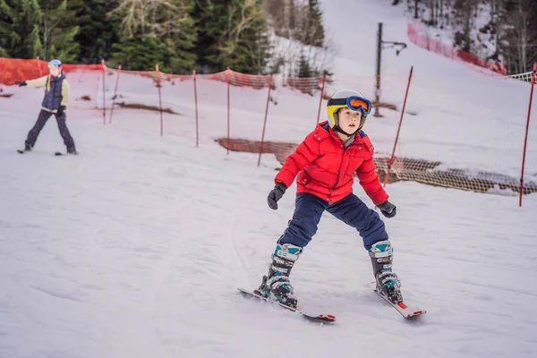 Esquí infantil en las montañas. Niño activo con casco de seguridad, gafas y bastones. Carrera de esquí para niños pequeños. Deportes de invierno para la familia. Clases de esquí para niños en la escuela alpina. Pequeño esquiador corriendo en la nieve — Foto de Stock